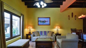 A living room with a sofa set, a coffee table, and two lamps. There is a painting on the wall and a ceiling fan. - Mission Gate 1A,  1-bedroom condo by Island House Vacation Rentals (West Bay)