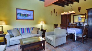 A living room with a sofa, armchair, and coffee table, a dining area with a table and chairs, and a kitchen area with a stove and cabinets. - Mission Gate 1A,  2-bedroom condo by Island House Vacation Rentals (West Bay)