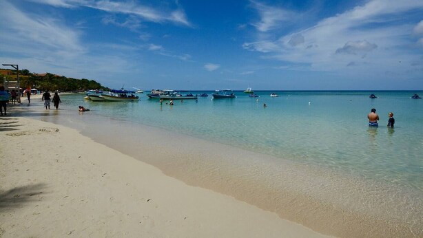 A beach with clear turquoise water, several boats, and people enjoying the shore. - Mission Gate 1A,  2-bedroom condo by Island House Vacation Rentals (West Bay)