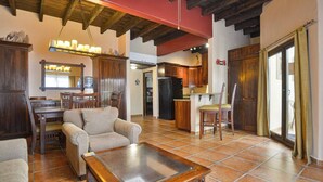 A spacious living room with a wooden coffee table, a sofa, and a dining area with wooden chairs and a table. - Mission Gate 3B, 2-bedroom condo by Island House Vacation Rentals (West Bay)