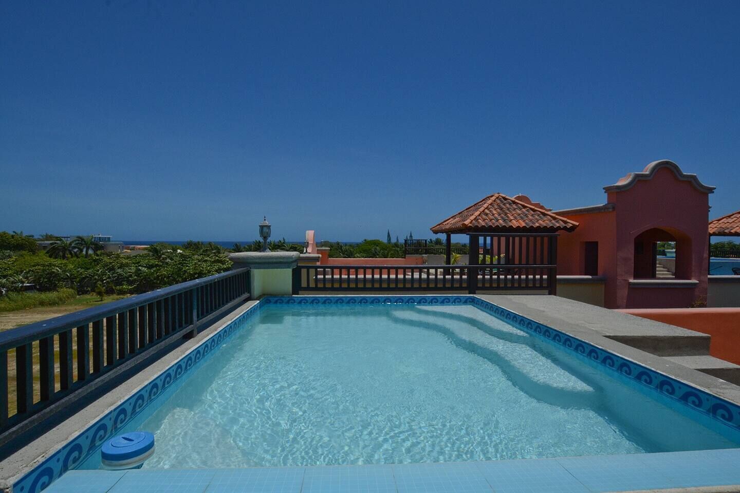 A swimming pool with a tiled edge, a gazebo, and a view of the ocean.
