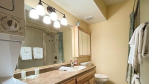 A bathroom with a sink, mirror, and toilet. There are towels hanging on the wall and a shower curtain.