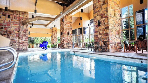 An indoor swimming pool with stone pillars, a covered seating area, and a view of the outdoors.