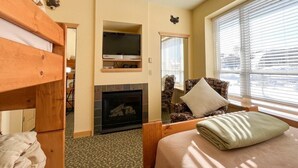 A cozy room with a bunk bed, a fireplace, a television, and a window with blinds.