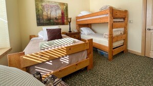 A room with two bunk beds, a ceiling fan, a painting on the wall, and a patterned carpet.