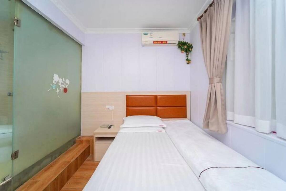 A single bed with a wooden headboard, a bedside table with a lamp, and a window with curtains.