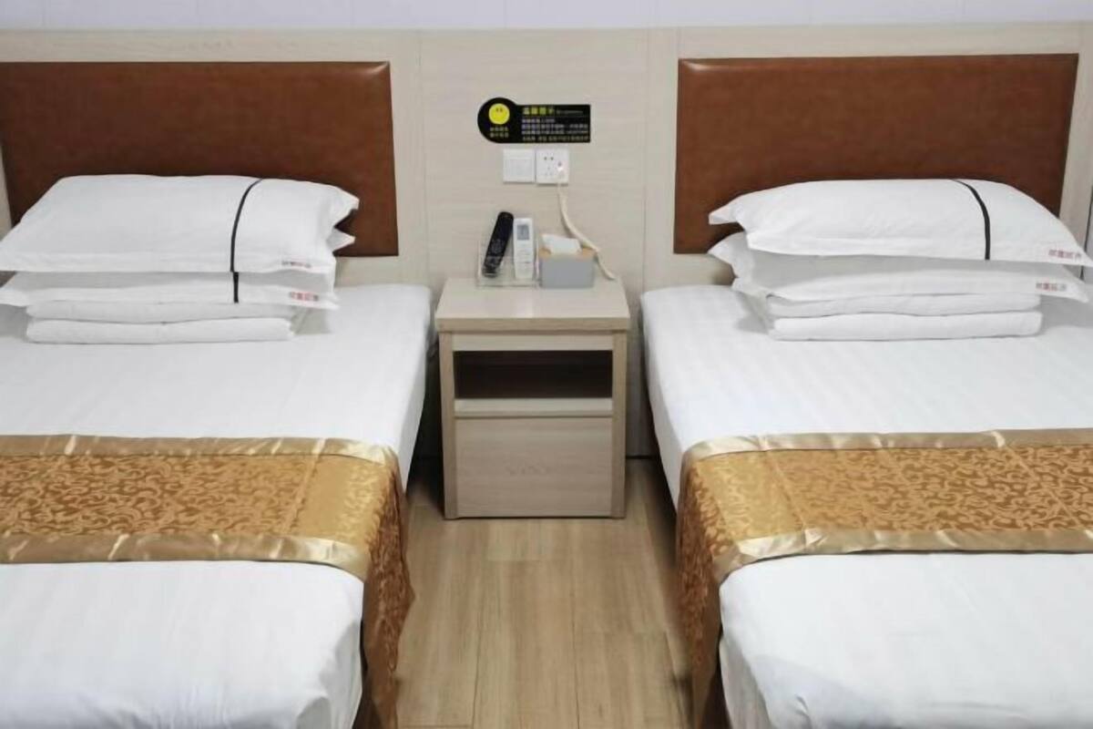 A hotel room with two beds, a bedside table with a phone and a small box, and a wall-mounted sign.