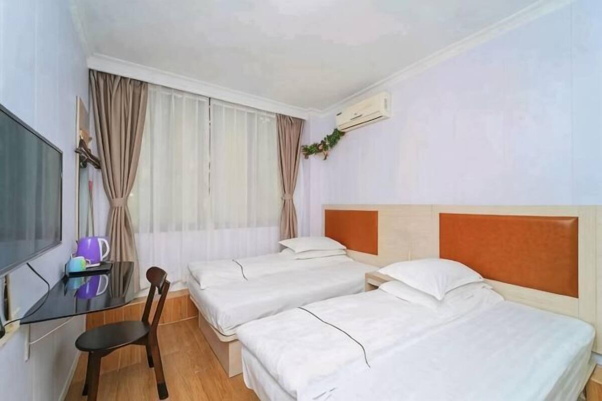 A hotel room with two beds, a desk with a chair, a TV, and a window with curtains.