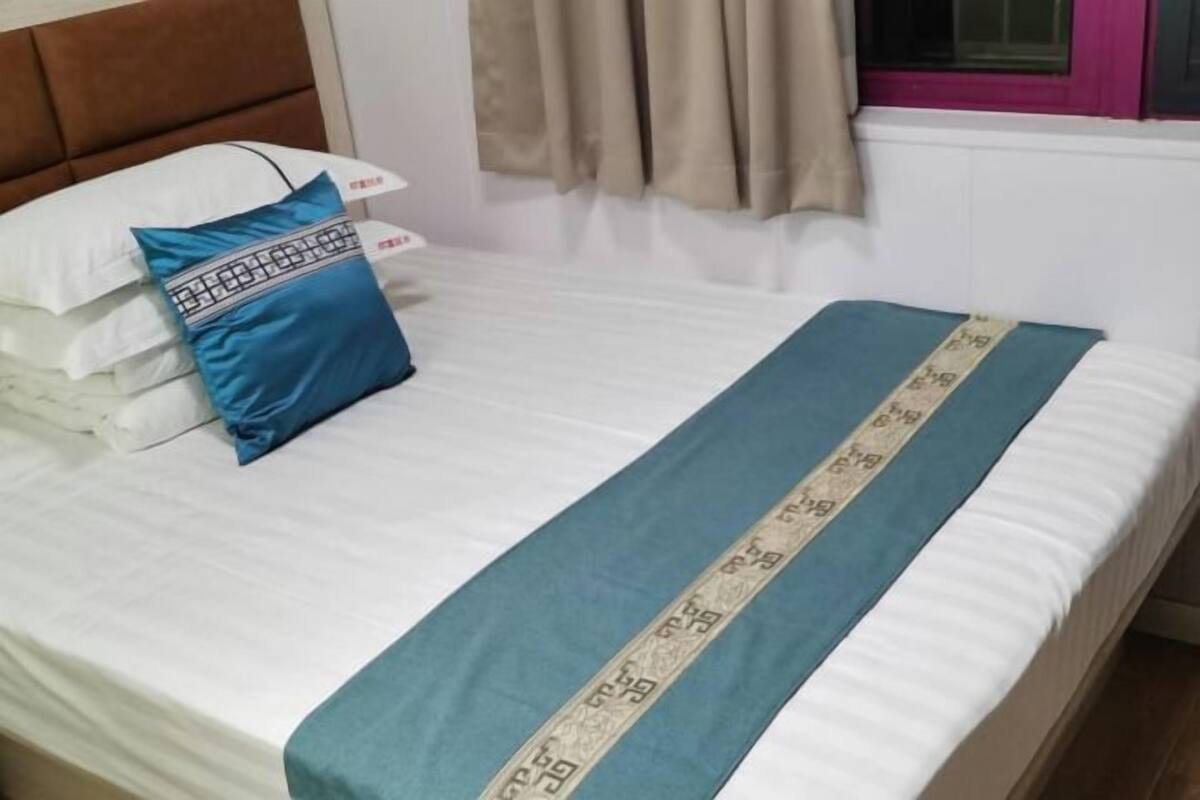 A bed with white bedding, a blue pillow, and a blue bedspread with a decorative border.