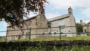 A stone building with a white balcony, surrounded by greenery and a stone wall. - Bank Cottage (Hope Valley)