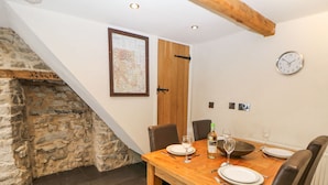 A dining area with a wooden table set for two, a bottle of wine, and a bowl. There is a clock on the wall and a framed map above the table. - Bank Cottage (Hope Valley)