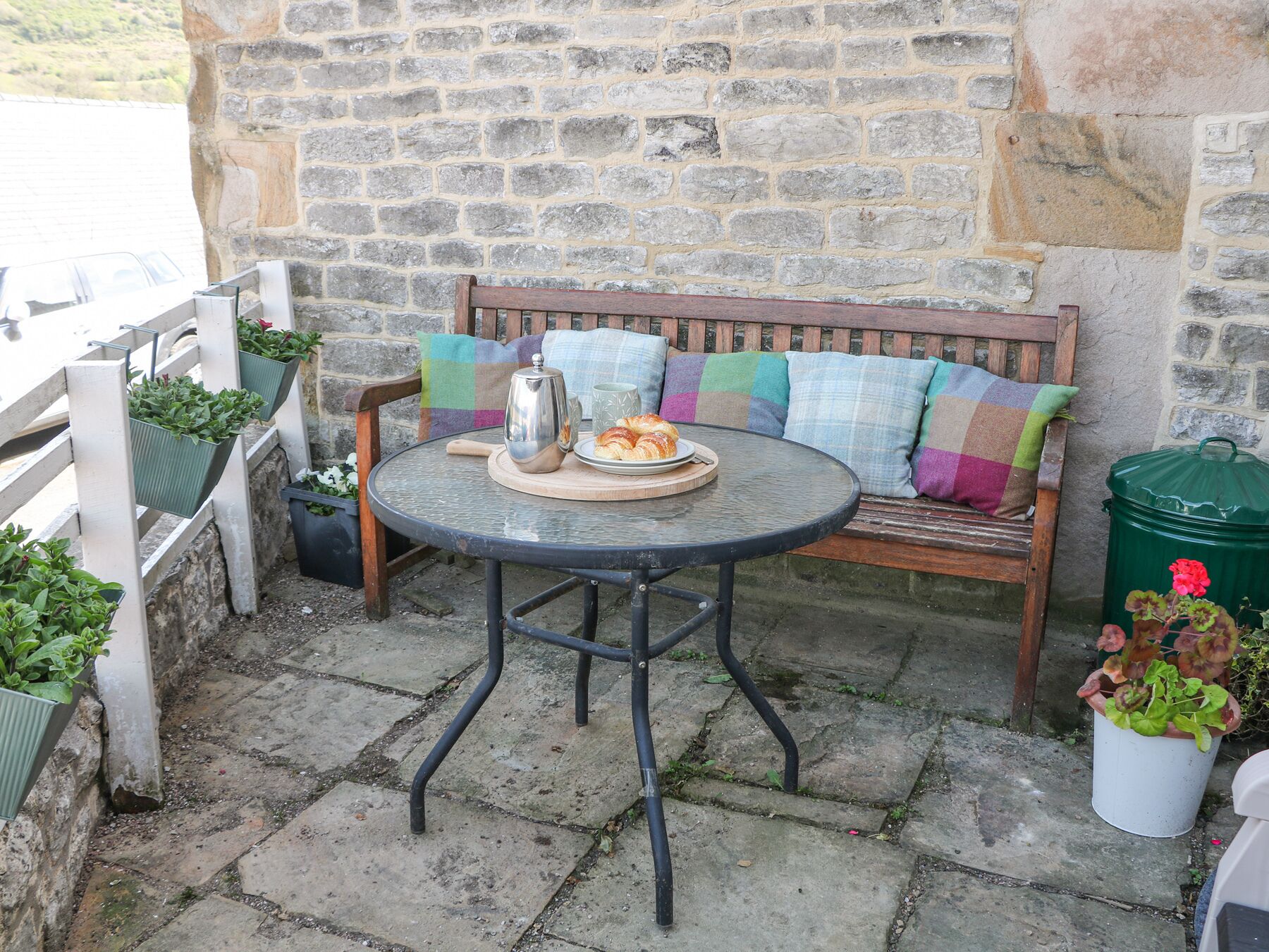 Un mur de pierre avec un banc en bois et une table ronde en métal.