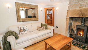 A cozy living room with a white sofa, a wooden coffee table, a fireplace, and a bookshelf. - Bank Cottage (Hope Valley)