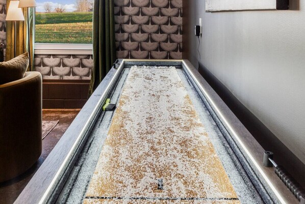 Una habitación con un espejo grande y polvoriento, un papel tapiz estampado, vistas a través de una ventana y una lámpara.