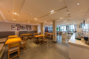 Un café moderne avec des tables et des chaises en bois, un comptoir équipé pour préparer le café et des tableaux encadrés accrochés aux murs.
