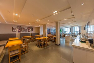 A modern cafe with wooden tables and chairs, a counter with coffee-making equipment, and framed pictures on the walls.