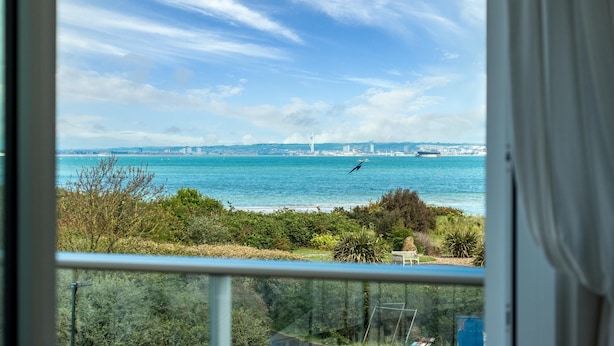 Une vue sur la côte depuis un balcon, avec un ciel dégagé, un oiseau en vol et une silhouette de ville en arrière-plan.