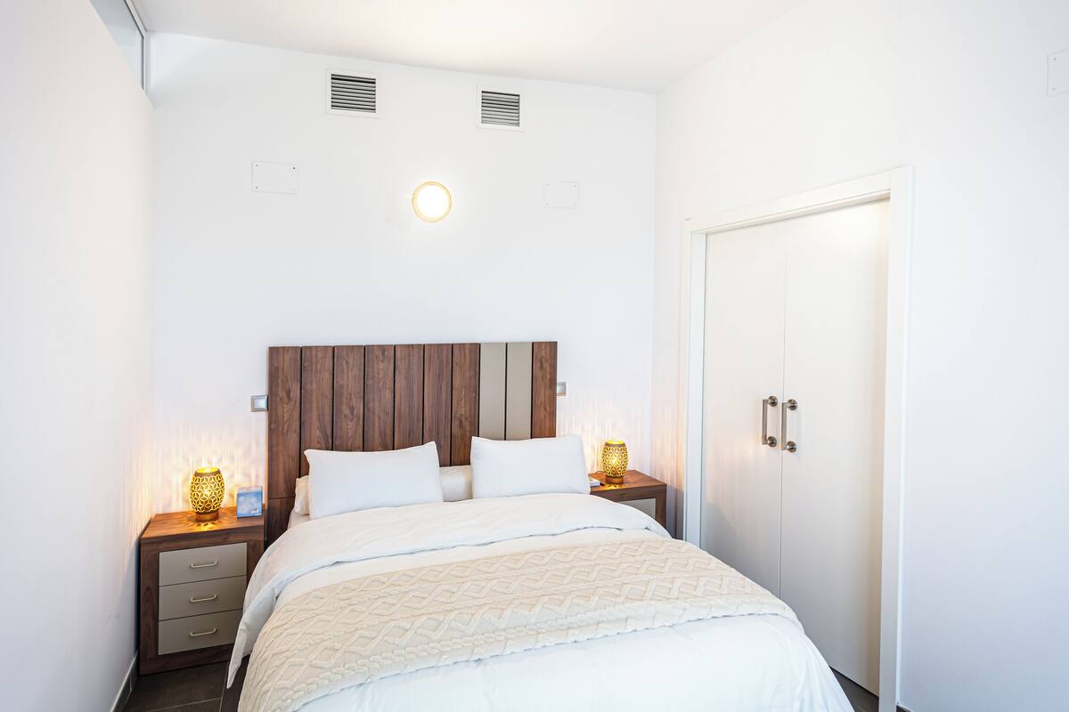 A neatly arranged bedroom with a wooden headboard, two bedside tables with lamps, a wardrobe, and a door.