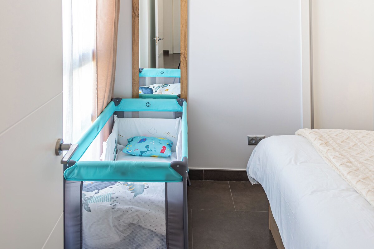 A bedroom with a crib, a bed, a mirror, and a window with curtains.