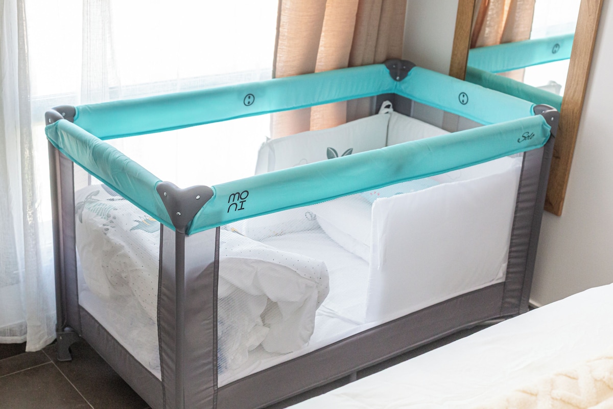 A baby crib with a mesh side and a solid side, equipped with a safety guard.