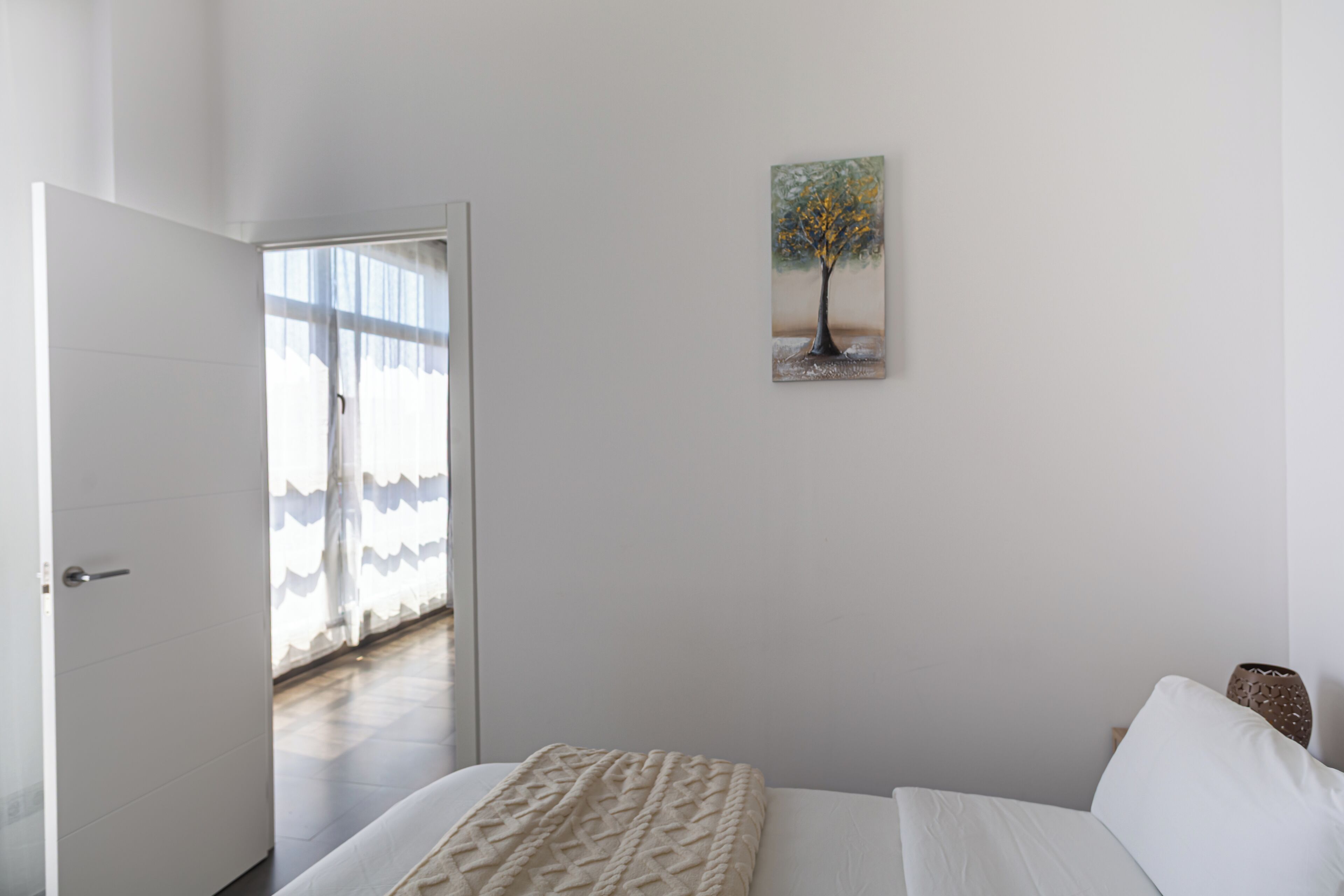 Une chambre à coucher avec un lit, un tableau représentant un arbre et une porte donnant sur un balcon.