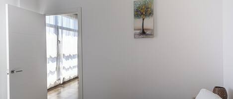 Une chambre à coucher avec un lit, un tableau représentant un arbre et une porte donnant sur un balcon.
