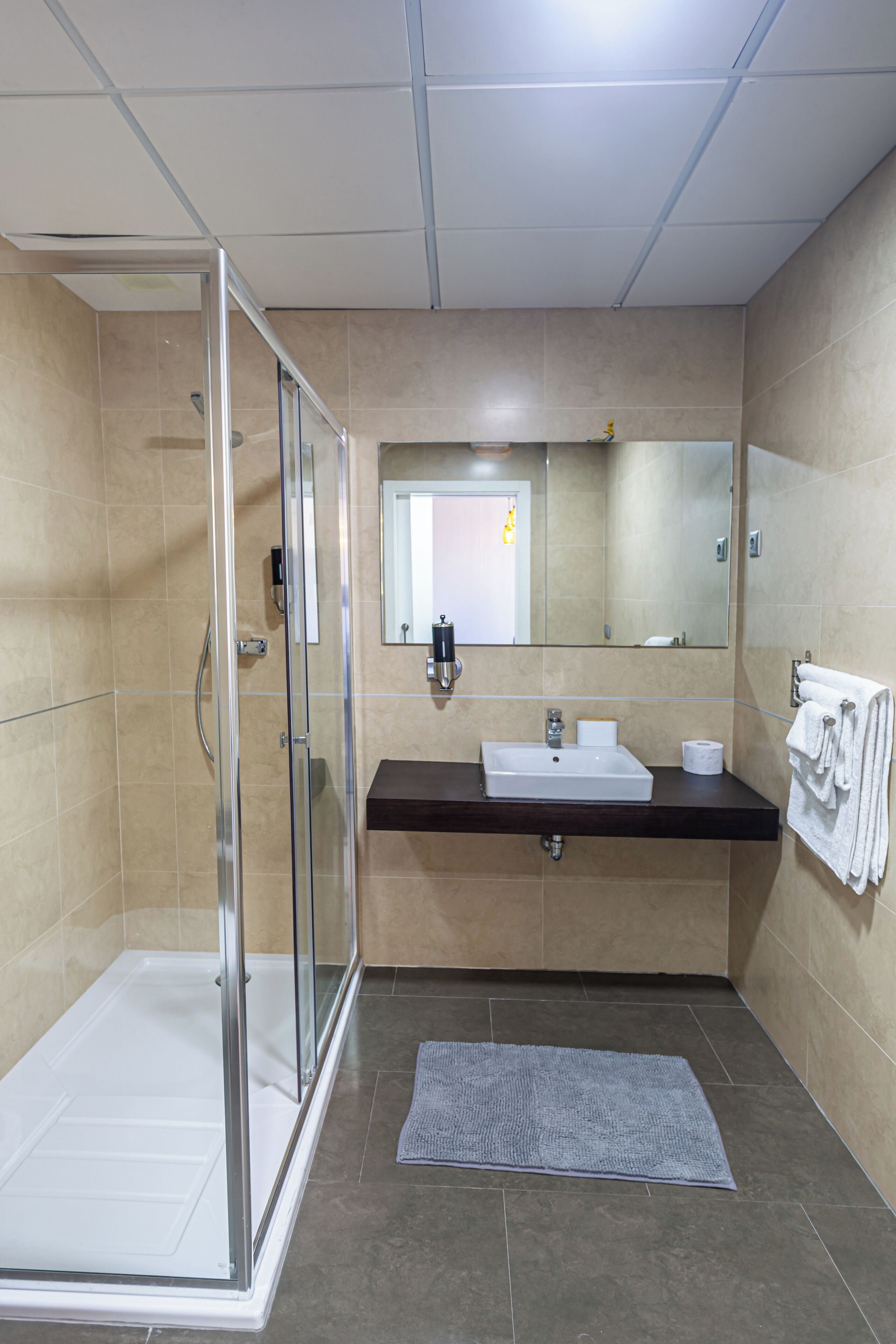 A modern bathroom with a glass-enclosed shower, a sink with a mirror above, and a towel rack on the wall.