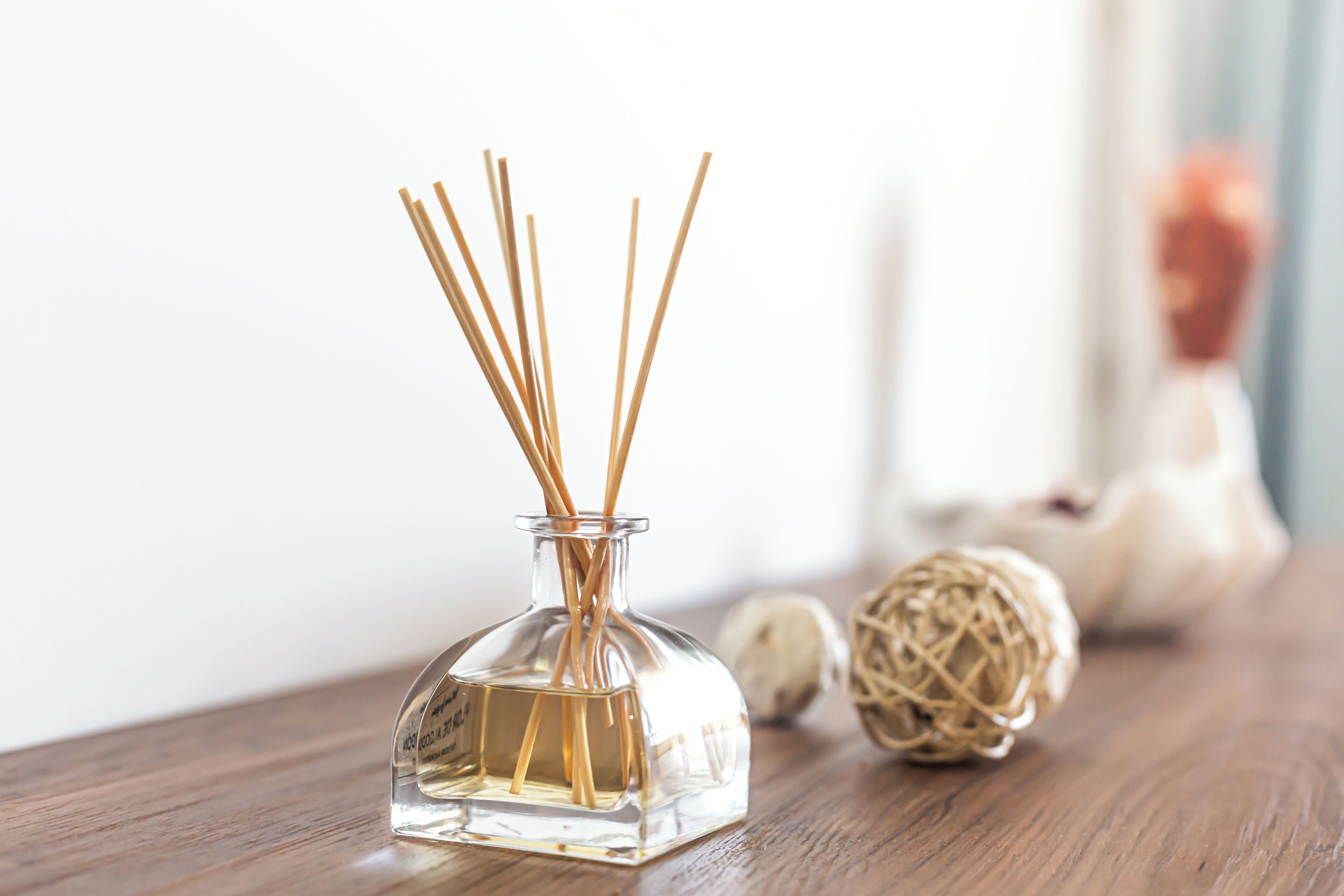 A clear glass bottle with reed sticks, placed on a wooden surface with a blurred background.