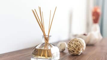 Una botella de vidrio transparente con palitos de junco, sobre una superficie de madera con un fondo desenfocado.