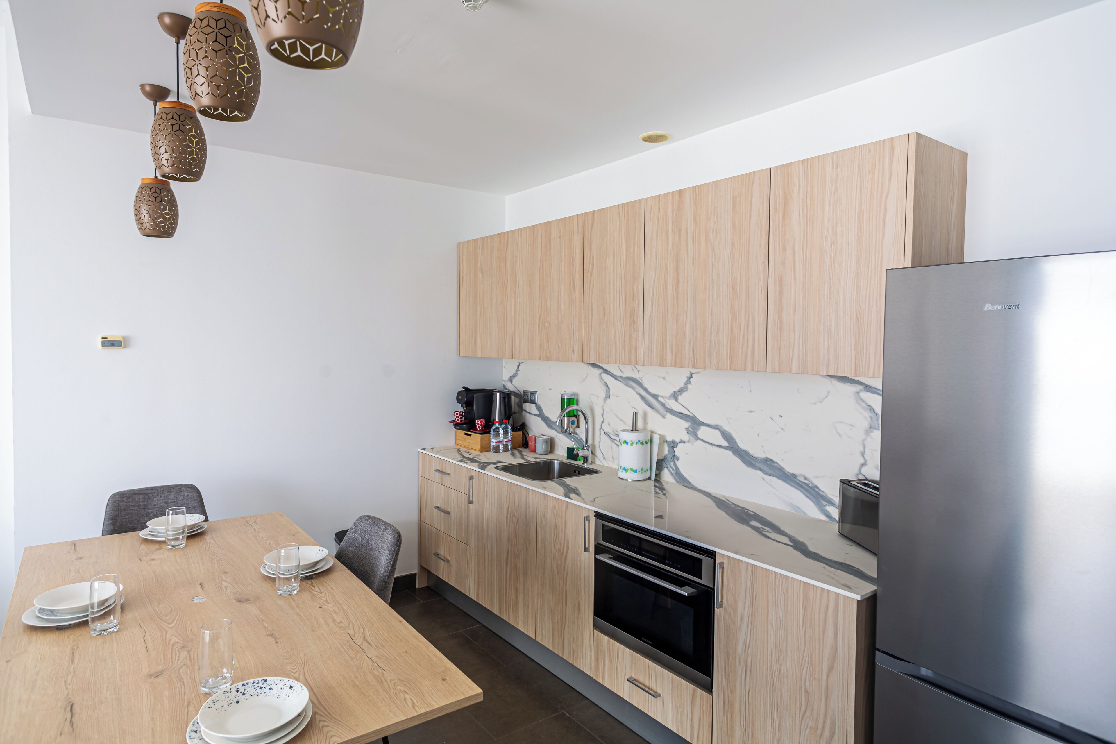 Eine moderne Küche mit Holzausstattung, einer Marmor-Spritzschutzwand und einem Edelstahl-Kühlschrank.