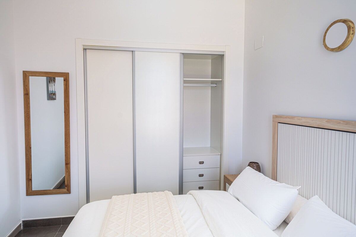 A bedroom with a bed, a wardrobe, a mirror, and a bedside table.