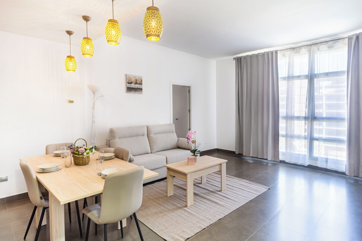 A modern living room with a sofa, dining table, and hanging pendant lights.
