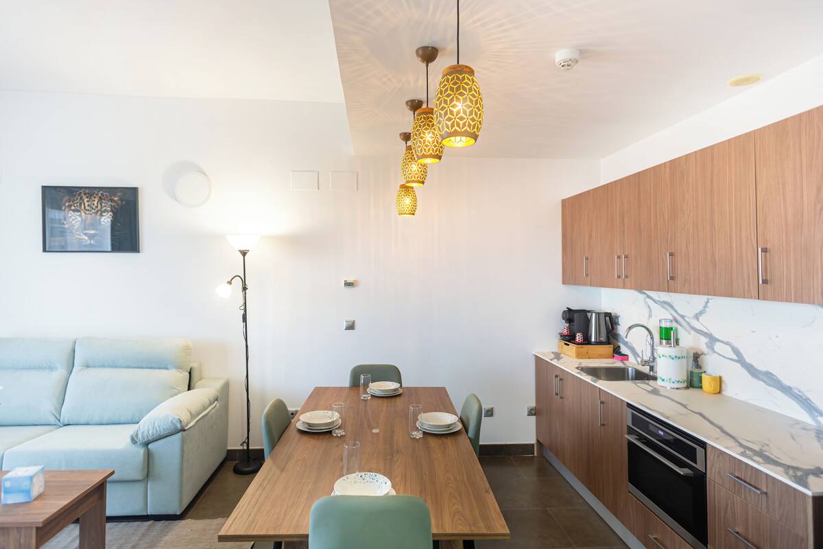A modern kitchen with wooden cabinets, a marble countertop, and a dining area with a wooden table and chairs.