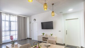 Un soggiorno moderno con zona pranzo, una TV a schermo piatto montata a parete e un'ampia finestra con tende.