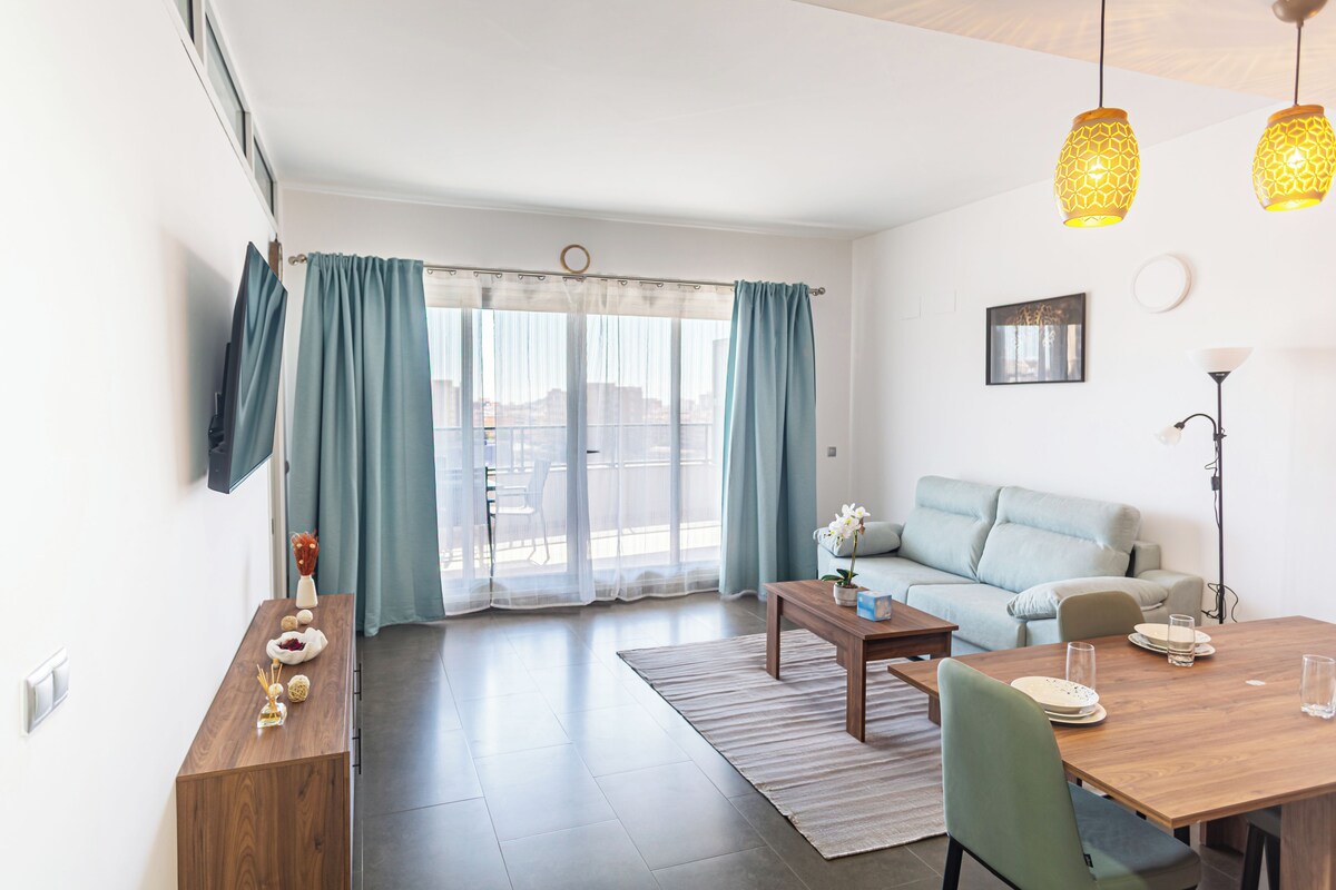 A modern living room with a sofa, dining table, and a TV mounted on the wall.