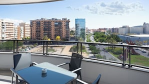 Un balcone con tavolo e sedie, affacciato su una città con edifici e una strada.
