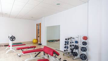 Un gimnasio con bancos de ejercicio, un soporte para pesas y una pelota de yoga.