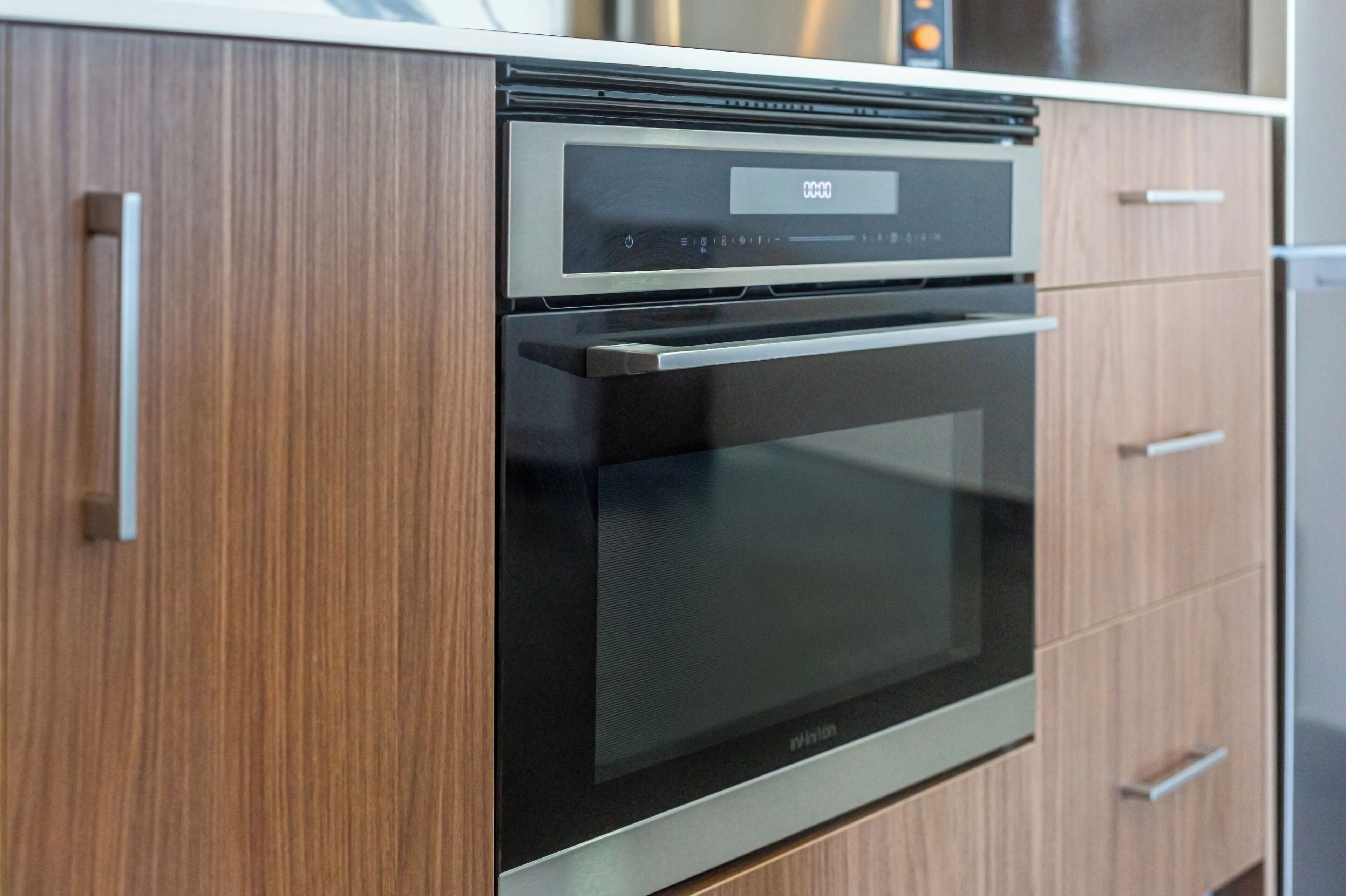 Una cocina moderna con horno empotrado y microondas, armarios de madera y encimera de acero inoxidable.