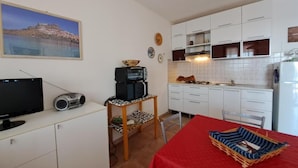 A compact kitchen with white cabinets, a microwave, and a coffee maker on a small table. There is a television on a cabinet and a red tablecloth on a dining table. - Casa Marina di Castelsardo (Castelsardo)