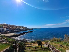 A coastal town with buildings along the shore, a clear blue sky, and a wooden fence in the foreground. - Casa Marina di Castelsardo (Castelsardo)