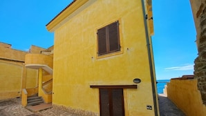 A yellow building with a window and a door, a staircase, and a stone-paved area. - Casa Marina di Castelsardo (Castelsardo)