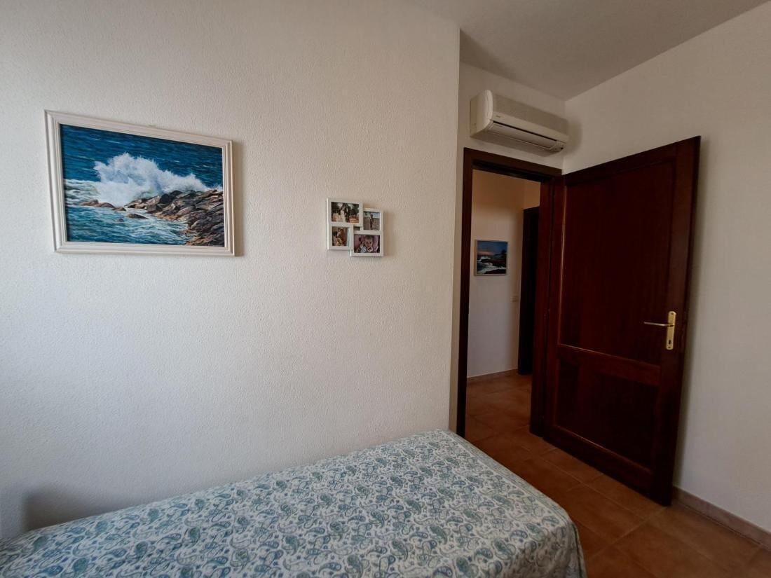 A room with a bed, a framed picture of the sea, a small photo collage, and a wooden door.
