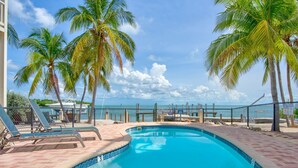 A swimming pool with lounge chairs, palm trees, and a view of the ocean. - Oceanview Rooftop Retreat  3BR 3BA in Marathon FL (Marathon)