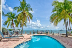 A swimming pool with lounge chairs, palm trees, and a view of the ocean. - Oceanview Rooftop Retreat  3BR 3BA in Marathon FL (Marathon)