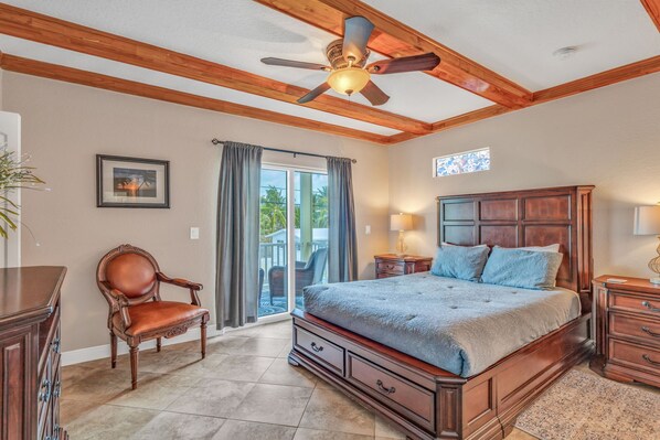 A bedroom with a large bed, wooden ceiling beams, a ceiling fan, a window with curtains, and a view of the outdoors. - Oceanview Rooftop Retreat 3BR 3BA in Marathon FL (Marathon)