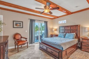 A bedroom with a large bed, wooden ceiling beams, a ceiling fan, a window with curtains, and a view of the outdoors. - Oceanview Villa w/ Private Rooftop & Pool (Marathon)