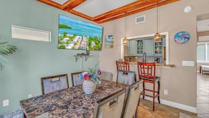 A dining area with a marble table, chairs, a vase of flowers, a painting, and a kitchen area with a hanging light.