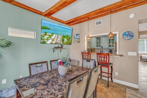 A dining area with a marble table, chairs, a vase of flowers, a painting, and a kitchen area with a hanging light. - Oceanview Rooftop Retreat  3BR 3BA in Marathon FL (Marathon)