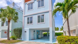 A multi-story residential building with a light blue exterior, a balcony with a red roof, and a small entrance area with a door and a wreath. - Oceanview Rooftop Retreat  3BR 3BA in Marathon FL (Marathon)