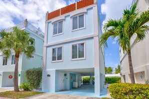 A multi-story residential building with a light blue exterior, a balcony with a red roof, and a small entrance area with a door and a wreath. - Oceanview Rooftop Retreat  3BR 3BA in Marathon FL (Marathon)